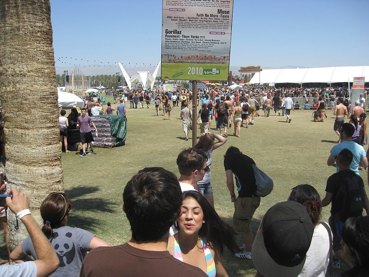 Festival-goers on the lawn near a set-times sign at Coachella 2010.